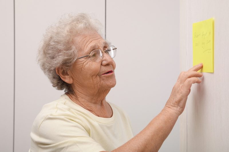 The old lady sticking the yellow color paper on a wall