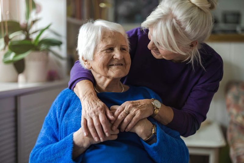 Daughter leaning and hugging elderly mother while caring for her.